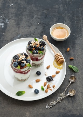 Yogurt oat granola with berries, honey and nuts in glass jars, dark grunge backdropの写真素材