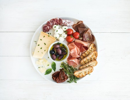 Cherry-tomatoes, parmesan cheese, meat variety, bread slices, dried tomatoes, olives and basil on...