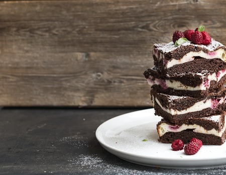 Brownies-cheesecake tower with raspberries on white ceramic plate, wooden backdrop, copy spaceの写真素材