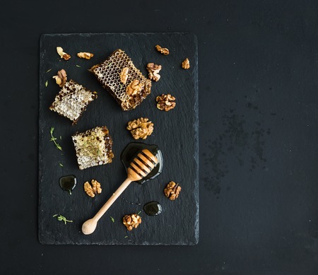 Honeycomb, walnuts and honey dipper on black slate tray over grunge dark backdrop, top view, copy spaceの写真素材
