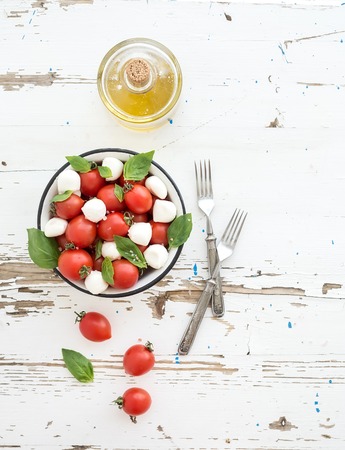 Caprese salad: cherry-tomatoes and mozzarella in metal bowl witholive oil on rustic white wooden backdrop, top view, copy spaceの写真素材
