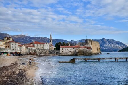 Budva, Montenegro, Balkan Peninsula, 25.01.2015. Budva beach near old town wall and fortress in winter season. People sitting in a cafe, children playing near the seaのeditorial素材