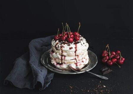 Pavlova cake with fresh cherry, cheese cream and chocolate chips in vintage silver plate over dark grunge backdropの写真素材