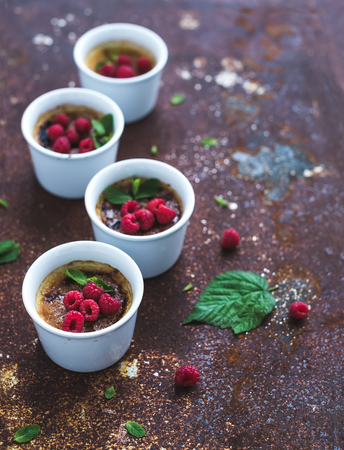 Creme brulees with raspberries and mint in white bowls over grunge metal backdrop. Top view, copy space, selective focusの写真素材