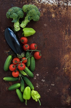 Vegetable mix of garden cherry tomatoes, cucumbers, paprikas, eggplant, broccoli on rusty metal grunge background, top view, copy spaceの写真素材