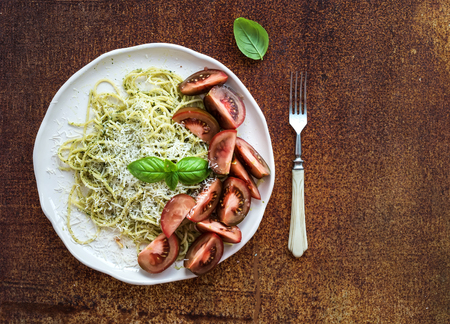 Pasta spaghetti with pesto sauce, basil and fresh kumato tomatoes on grunge rusty metal backdrop, top view, copy spaceの写真素材