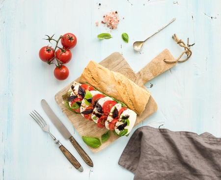 Tomato, mozzarella and basil sandwich on wooden chopping board over light blue background, top viewの写真素材