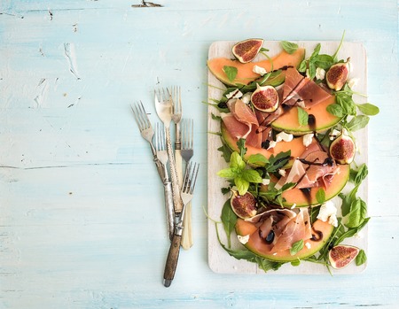 Prosciutto, melon, fig and soft cheese salad on a white serving board over grunge background, top view, copy spaceの写真素材