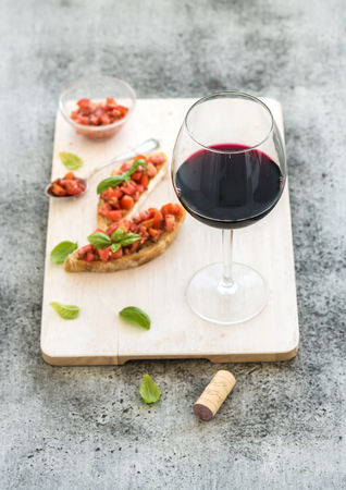 Wine appetizer set. Glass of red wine, brushettas with fresh tomato and basil on over rustic grunge grey backdropの写真素材