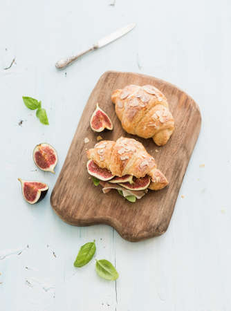 Freshly baked croissants with fresh figs and prosciutto on serving board over blue rustic wooden backdrop, top view, selective focusの写真素材