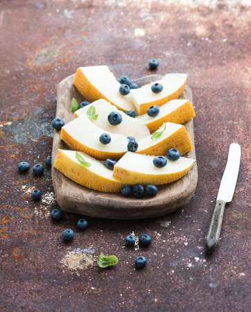 Melon and blueberries in a rustic wooden serving dish over grunge metal rusty background, top viewの写真素材