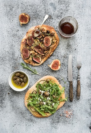 Rustic homemade pizzas with eggpant, cheese, olives, arugula, prosciutto and figs over grunge backdrop. Top viewの写真素材