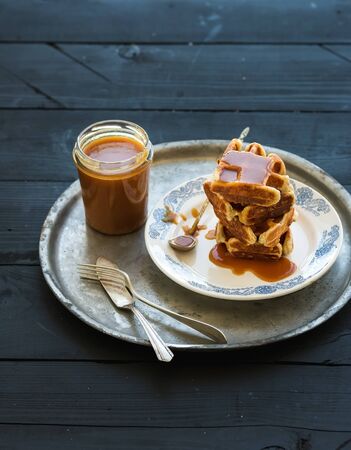 Stack of Belgian soft waffles with salted caramel sauce on vintage silver tray over black wooden background, selective focusの写真素材