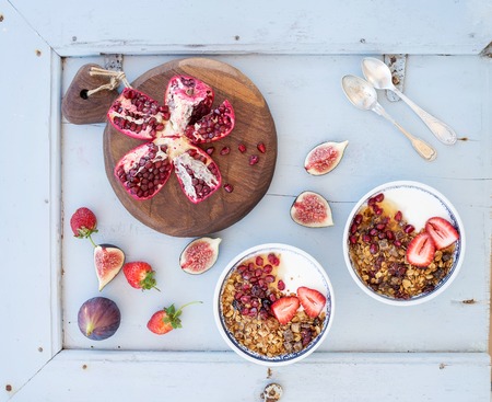 Healthy breakfast set. Bowls of oat granola with yogurt, fresh strawberries, figs, pomegranate andd  honey over light blue wooden backdrop, top viewの写真素材