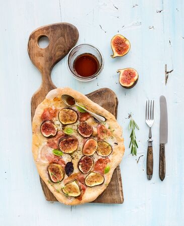 Rustic homemade pizza with figs, prosciutto and mozzarella cheese on dark wooden serving board over...