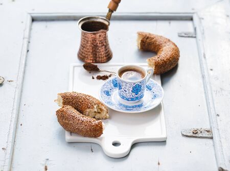 Turkish black coffee served in traditional ceramic cup with pattern, sesame bagel called simit on...