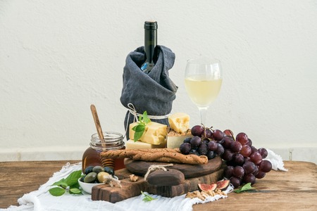 Glass of white wine, cheese board, grapes,fig, strawberries, honey and bread sticks  on rustic wooden table, light background, selective focusの写真素材