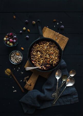 Healthy breakfast. Oat granola crumble with frozen fresh berries, and seeds in irom skillet pan on rustic wooden board over dark backdrop, top viewの写真素材