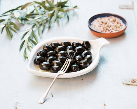 Black olives in white ceramic plate, branches and spices over light blue background, selective focusの写真素材