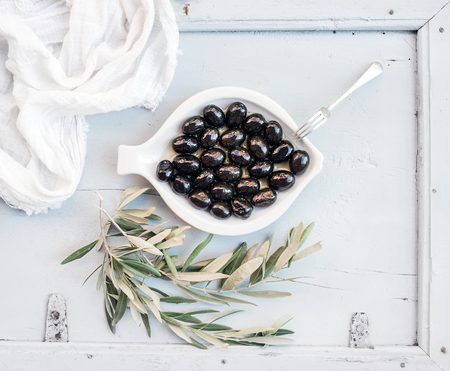 Black Mediterranean olives in white ceramic plate with tree branches, top view.の写真素材