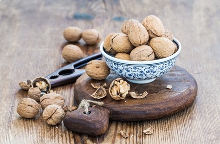 Walnuts in ceramic bowl and on wooden board with nutcracker over  rustic wooden background,...
