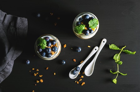 Healthy breakfast set. Yogurt oat granola with blueberries and mint leaves in glass jars on black backdrop, top viewの写真素材