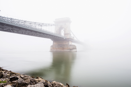 Chain Bridge over the Danube and a boat in Budapest, Hungary, in evening lights, on a foggy day. Shot from the Pest side of the Danube riverの写真素材