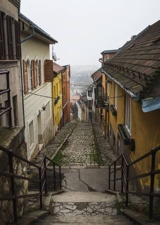 Old medieval narrow stone paved street in Buda district of of Budapest on a foggy day in winter....