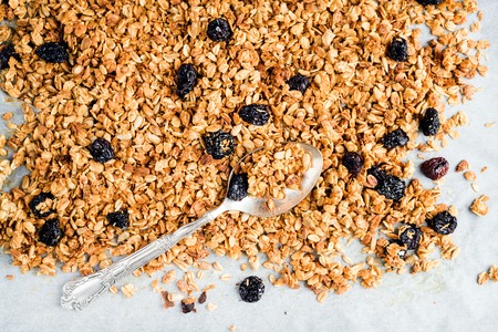 Homemade oat, cherry and coconut granola over baking paper with spoon, top view