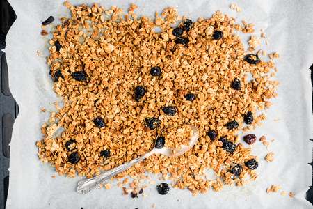 Homemade oat, cherry and coconut granola over baking paper with spoon, top viewの写真素材