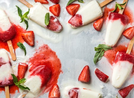 Strawberry yogurt ice cream popsicles with mint over steel tray background. Top view, copy space....