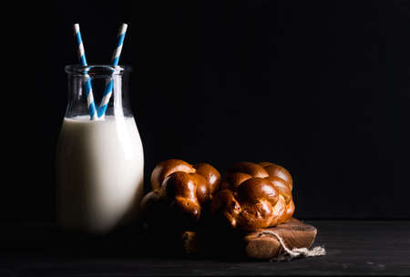 Bottle of milk and milk loaf buns on rustic wooden board over dark background, selective focus, copy spaceの写真素材