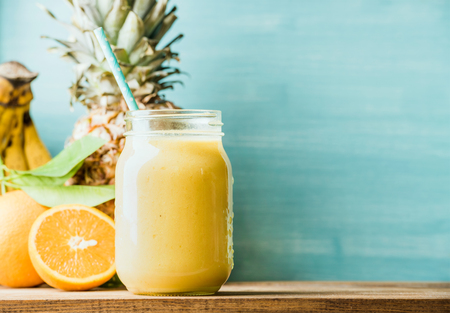 Freshly blended yellow and orange fruit smoothie in glass jar with straw. Turquoise blue background, copy spaceの写真素材