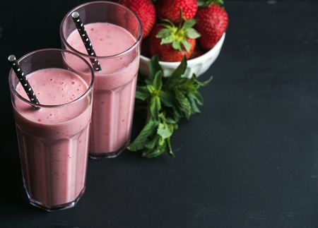Strawberry and mint smoothie in tall glasses, bawl of fresh berries on dark rustic wood background. Selective focus, copy spaceの写真素材