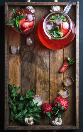 Homemade strawberry lemonade with mint and ice, served with fresh berries on rustic wooden tray over dark background, top view, copy space, vertical compositionの写真素材