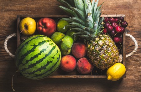 Summer friut variety in wooden tray over wooden background, top view. Watermelon, pineapple, lemon, figs, peach, sweet cherry, appleの写真素材
