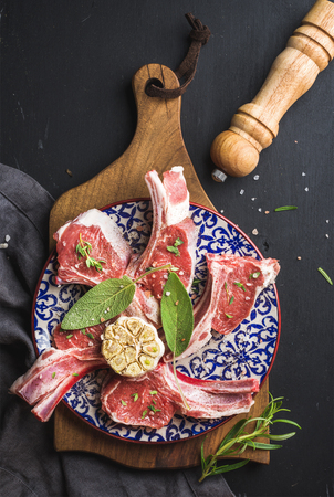 Raw uncooked lamb chops with herbs and spices on wooden board over dark wooden background, top view, vertical compositionの写真素材