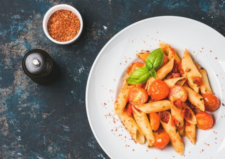 Pasta penne with tomato sauce, basil and roasted tomatoes. Old painted dark plywood background, top view, copy space, horizontal compositionの写真素材