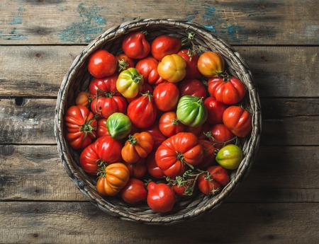 Fresh colorful ripe Fall heirloom tomatoes in basket over wooden background, top view, horizontal compositionの写真素材