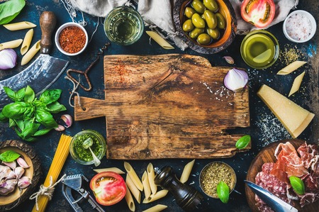 Italian food cooking ingredients on dark background with rustic wooden chopping board in center, top view, copy spaceの写真素材