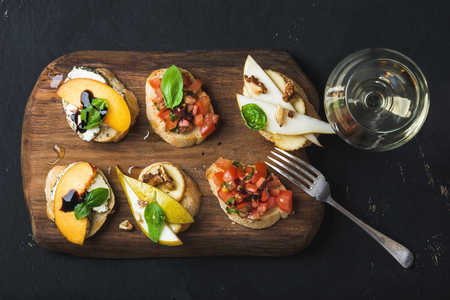 Bruschetta set with glass of white wine. Black plywood background, top view, horizontal compositionの写真素材