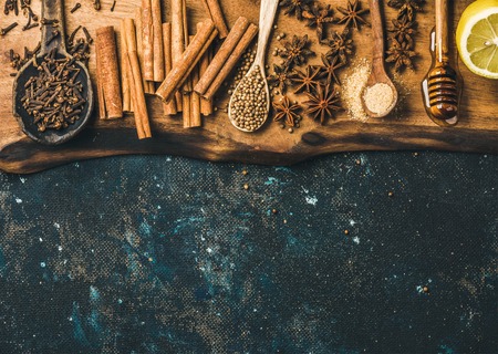 Ingredients for cooking mulled wine. Spices, honey, sugar and lemon on wooden board over old dark blue painted plywood background. Top view, copy spaceの写真素材