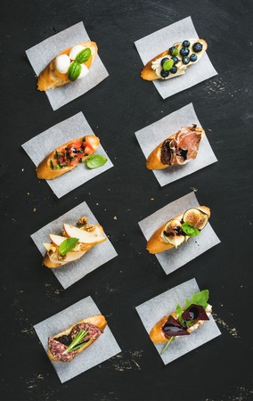 Italian crostini with various toppings on white baking paper over black plywood background, top viewの写真素材