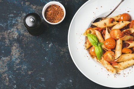 Pasta penne with tomato sauce, basil and roasted tomatoes. Old painted dark plywood background, top view, copy space, horizontal compositionの写真素材
