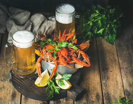 Two pints of wheat beer and boiled crayfish in metal pan served with with lemon and parsley on dark round serving board over rustic wooden background, selective focus, copy spaceの写真素材