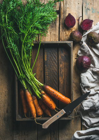 Healthy food cooking background. Vegetable ingredients. Fresh garden carrots and beetroots in wooden tray over rustic wooden background, top view, copy space, vertical compositionの写真素材