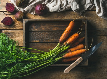 Healthy food cooking background. Vegetable ingredients. Fresh garden carrots and beetroots in wooden tray over rustic wooden background, top view, copy space, horizontal compositionの写真素材