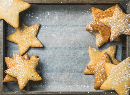 Sweet Christmas holiday gingerbread cookies in shape of stars with sugar powder on baking paper in rustic wooden tray, top view, copy space, horizontal compositionの写真素材