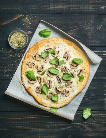 Homemade mushroom pizza with basil leaves and spices in glass on baking paper over dark scorched wooden background, top view, vertical compositionの写真素材