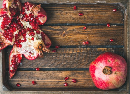 Fresh ripe seasonal pomegranates, one cut in pieces in rustic wooden tray, top view, copy space, horizontal compositionの写真素材